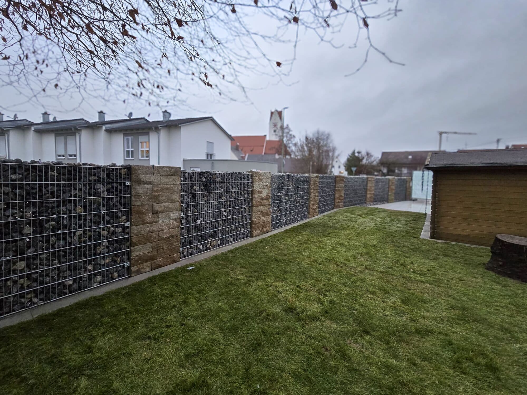 Gabionenwand mit Steinpfeilern als Grundstücksgrenze am Rasen