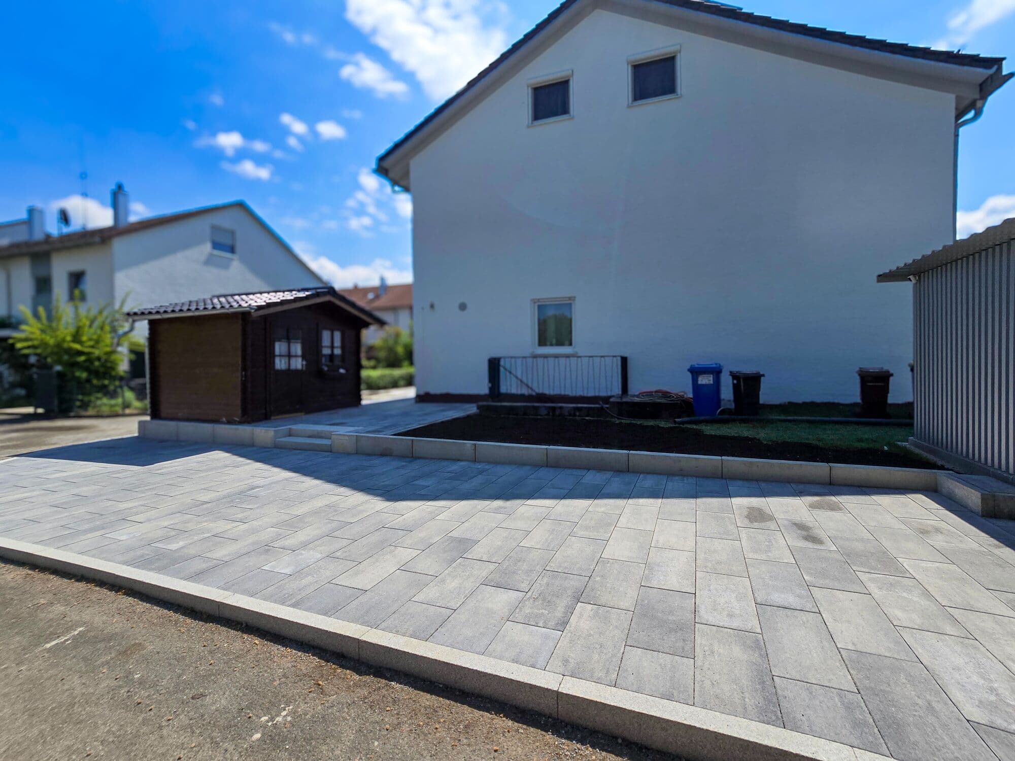 Gepflasterte Einfahrt in Grautönen neben einem Wohnhaus