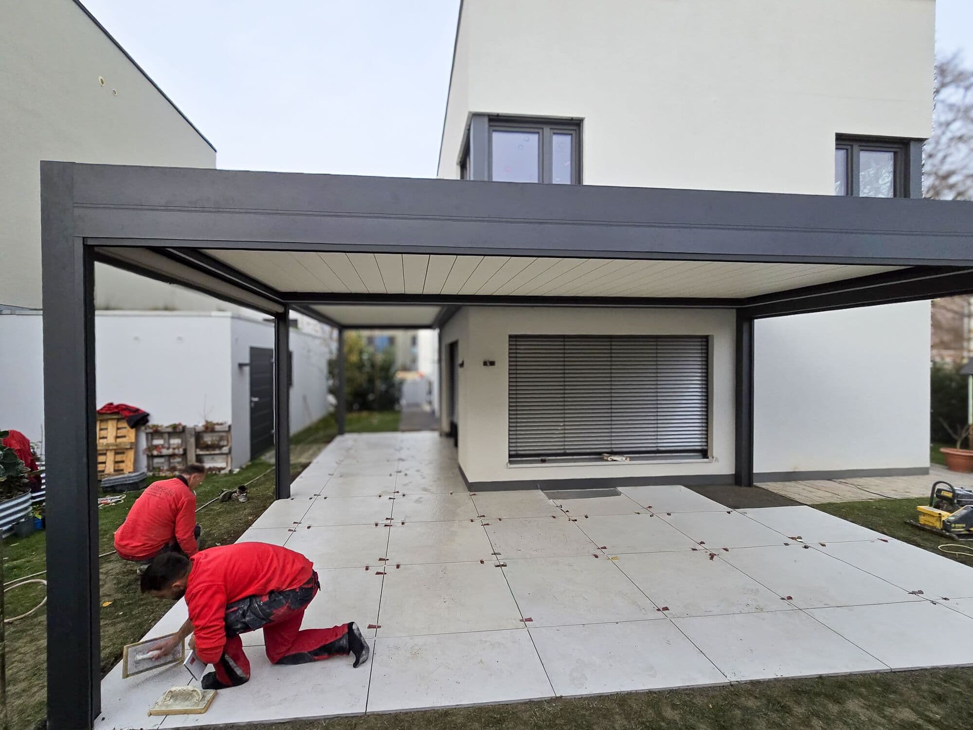 Zwei Mitarbeiter verlegen Großformatplatten unter einer Pergola